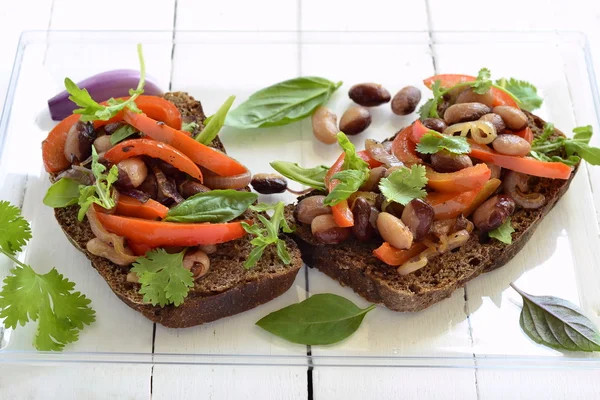 Rye bruschetta with beans, sweet peppers, arugula and red onion — Stock Photo, Image