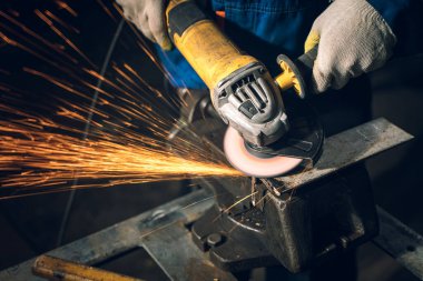 Özel kıyafet ve gözlüklü bir çilingir üretim işinde çalışıyor. Açı öğütücüyle metal işleme. Metal işçiliğinde kıvılcımlar