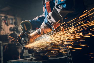 Özel kıyafet ve gözlüklü bir çilingir üretim işinde çalışıyor. Açı öğütücüyle metal işleme. Metal işçiliğinde kıvılcımlar