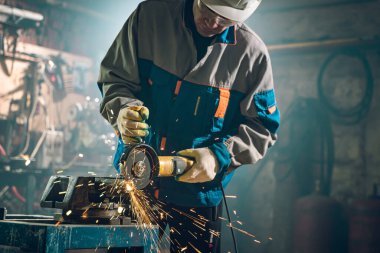 Özel kıyafet ve gözlüklü bir çilingir üretim işinde çalışıyor. Açı öğütücüyle metal işleme. Metal işçiliğinde kıvılcımlar
