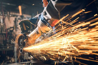 Özel kıyafet ve gözlüklü bir çilingir üretim işinde çalışıyor. Açı öğütücüyle metal işleme. Metal işçiliğinde kıvılcımlar