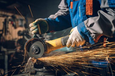 Özel kıyafet ve gözlüklü bir çilingir üretim işinde çalışıyor. Açı öğütücüyle metal işleme. Metal işçiliğinde kıvılcımlar