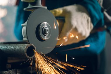 Özel kıyafet ve gözlüklü bir çilingir üretim işinde çalışıyor. Açı öğütücüyle metal işleme. Metal işçiliğinde kıvılcımlar