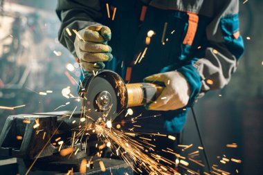 Özel kıyafet ve gözlüklü bir çilingir üretim işinde çalışıyor. Açı öğütücüyle metal işleme. Metal işçiliğinde kıvılcımlar