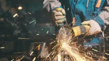 Özel kıyafet ve gözlüklü bir çilingir üretim işinde çalışıyor. Açı öğütücüyle metal işleme. Metal işçiliğinde kıvılcımlar