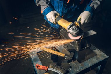 Özel kıyafet ve gözlüklü bir çilingir üretim işinde çalışıyor. Açı öğütücüyle metal işleme. Metal işçiliğinde kıvılcımlar