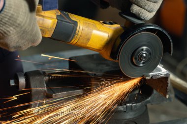 Özel kıyafet ve gözlüklü bir çilingir üretim işinde çalışıyor. Açı öğütücüyle metal işleme. Metal işçiliğinde kıvılcımlar