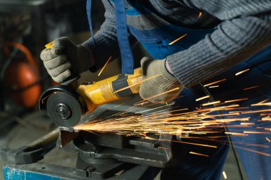Özel kıyafet ve gözlüklü bir çilingir üretim işinde çalışıyor. Açı öğütücüyle metal işleme. Metal işçiliğinde kıvılcımlar