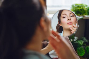 Genç ve güzel bir kadın aynaya bakarken evde makyaj yapıyor.