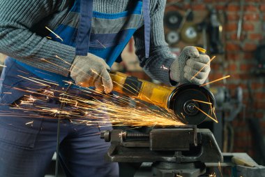 Özel kıyafet ve gözlüklü bir çilingir üretim işinde çalışıyor. Açı öğütücüyle metal işleme. Metal işçiliğinde kıvılcımlar