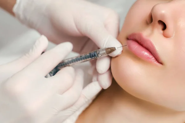 Lip augmentation and correction procedure in a cosmetology salon. The specialist makes an injection in the patient lips.
