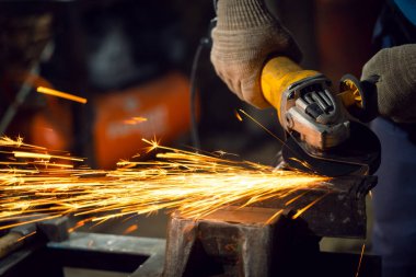 Özel kıyafet ve gözlüklü bir çilingir üretim işinde çalışıyor. Açı öğütücüyle metal işleme. Metal işçiliğinde kıvılcımlar