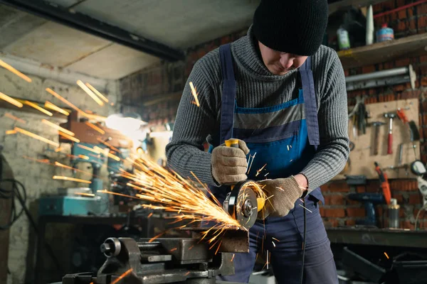 Il fabbro in abiti speciali e occhiali lavora in produzione. Lavorazione dei metalli con smerigliatrice angolare. Scintille nella lavorazione dei metalli — Foto Stock