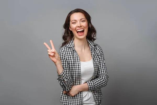 Portret van een lachende vrouw met een overwinningsbord en kijkend in een camera geïsoleerd op een grijze achtergrond — Stockfoto