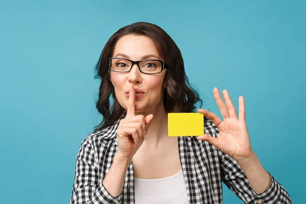 Schattige glimlachende vrouw in jurk shirt en bril, tonen credit card in de hand voor financiële en cashless samenleving concept, poseren op blauwe achtergrond. Kopieerruimte. — Stockfoto