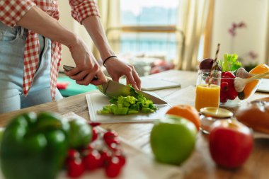 Yakın plan çekimde sadece salata dilimleyen bir kadın kırmızı biberli ve brokolili sağlıklı bir organik vejetaryen yemeğine hazırlanıyor. Mutfağın arka planında...