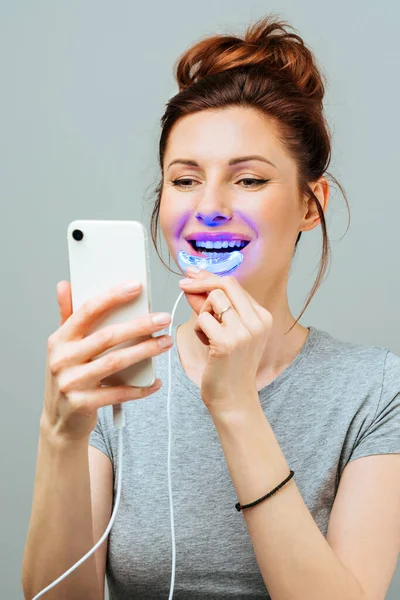 Una giovane donna è impegnata nello sbiancamento dei denti a casa. Complesso per sbiancamento dei denti con lampada UV — Foto Stock