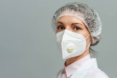 Gri arka planda tıbbi maske takan mutsuz genç bir doktorun portresi. Doktorlar yorgun gözlerle baktı. Koronavirüs konsepti.
