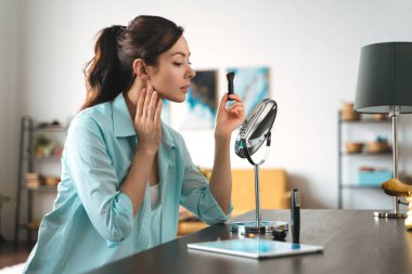 Genç ve güzel bir kadın aynaya bakarken evde makyaj yapıyor.