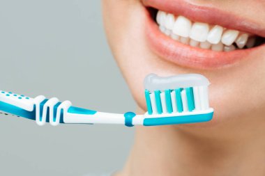 Sağlıklı beyaz dişleri olan bir kadın diş fırçası tutuyor ve gülümsüyor. Ağız temizliği kavramı