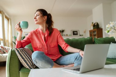Evdeki kanepede oturan mutlu genç kadın. Kadın çay içiyor..