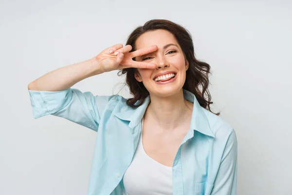 Portret van een lachende vrouw met een overwinningsbord en kijkend in een camera geïsoleerd op een witte achtergrond. — Stockfoto