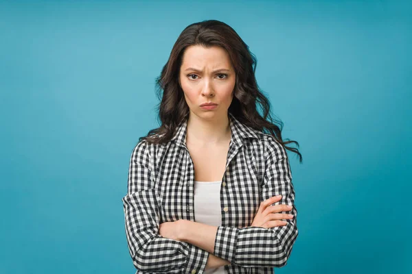 Portret van een boze jonge vrouw die over een geïsoleerde blauwe achtergrond staat. Kijkend naar de camera. — Stockfoto