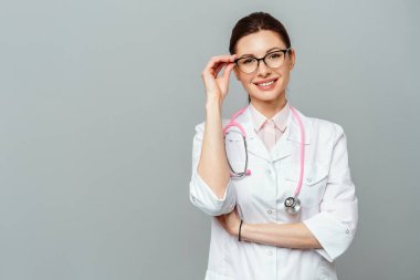 Dost canlısı gülümseyen genç bir bayan doktorun portresi. Gözlüklü bir kadın doktor resmi. Gri bir arkaplanda izole edilmiş.