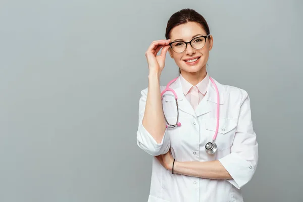 Portret van een vriendelijke lachende jonge vrouwelijke arts. Afbeelding van een vrouwelijke arts met bril. Geïsoleerd op een grijze achtergrond. — Stockfoto