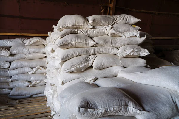 Large cloth bags with unknown bulk contents are lying in the warehouse. An image illustrating the products confiscated due to sanctions, or the capture of smugglers with illegal goods.