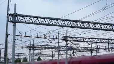 Kırmızı trenin üzerinde metal elektrik hatları asılı.