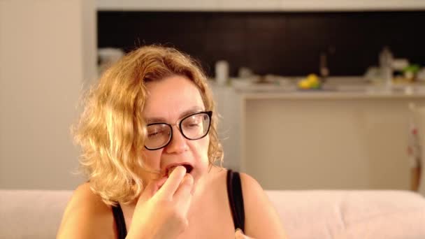 Mujer regordeta pone nueces marrones en la boca sentado en casa — Vídeo de stock