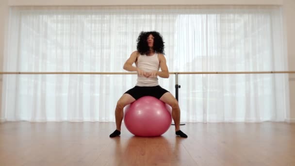 Svalnatý chlap v černé paruce skoky na cvičení míč v tělocvičně — Stock video