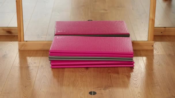 Жінка кладе кольорові рулонні килимки на коричневу дерев'яну підлогу в спортзалі — стокове відео