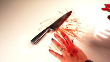 Eli kanlı genç bir kadın gümüş bıçağı beyaz masaya koyar.