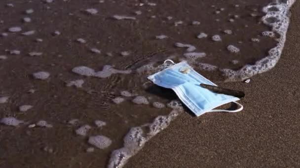 Masque jetable bleu se trouve sur la plage de sable humide jaune — Video