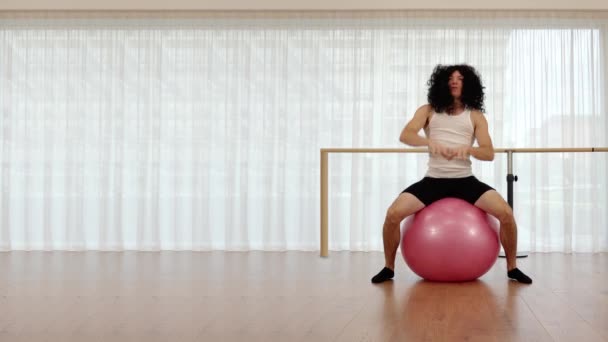 Muskulös kille med långa peruker sträcker sig på rosa träningsboll — Stockvideo