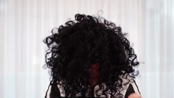 Guy dává na černé kudrnaté vlasy paruku pod jasným elektrickým světlem — Stock video