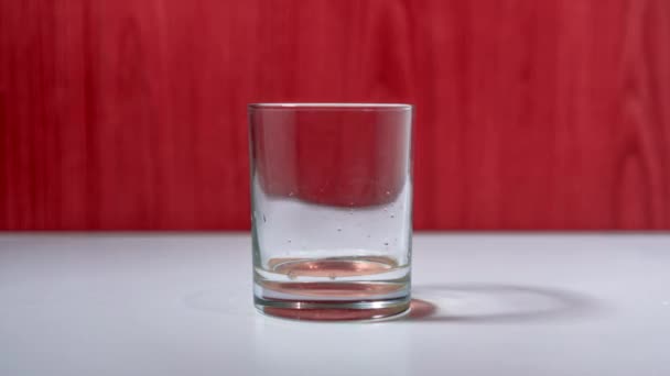 Vidro transparente enche com líquido em pé na mesa branca — Vídeo de Stock