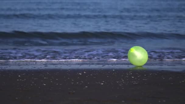 Green air balloon rolls past running ocean waves on beach — Stok video