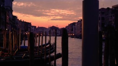 Tahta sütunlara bağlı uzun gondol siluetleri.