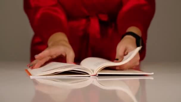 Молода жінка в червоному халаті перетворює сторінки паперових книг руками — стокове відео