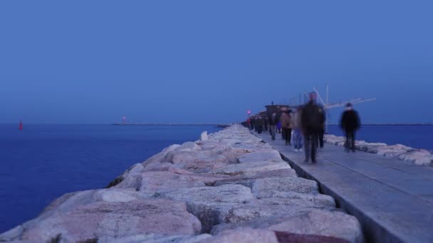 People walk along pier near tranquil sea in autumn evening — Stock Video