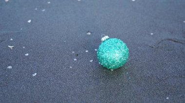 Kadın ıslak kumdan düşen yeşil Noel ağacı topunu alır.