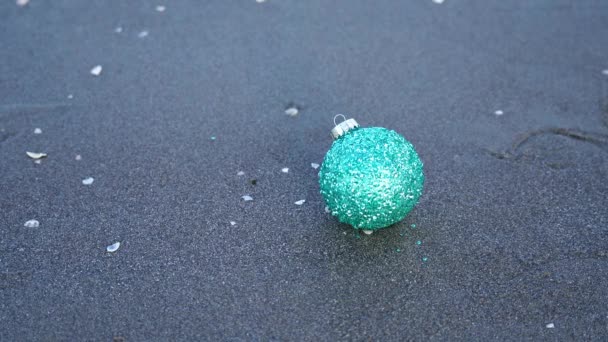 女はぬれた砂から落ちる緑のクリスマスツリーボールを取ります — ストック動画