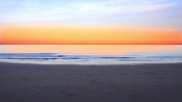 Okyanus dalgaları, parlak turuncu günbatımında boş kumsalda akıyor. — Stok video