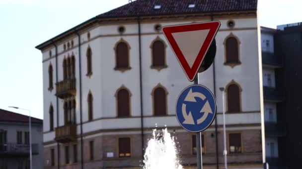 Znaki drogowe umieszczone na ulicy przed budynkiem i fontanną — Wideo stockowe