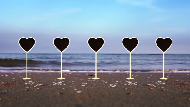 Ensemble de plaques en forme de coeur se tient sur le sable humide de la plage de l'océan — Video