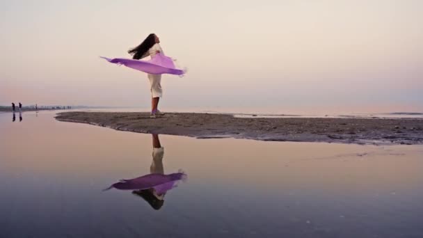 Glückliche Frau im weißen warmen Kleid tanzt mit Schal am Strand — Stockvideo