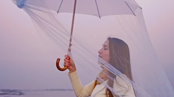 Pani w bieli spacery pod parasolem z długim welonem na plaży — Wideo stockowe
